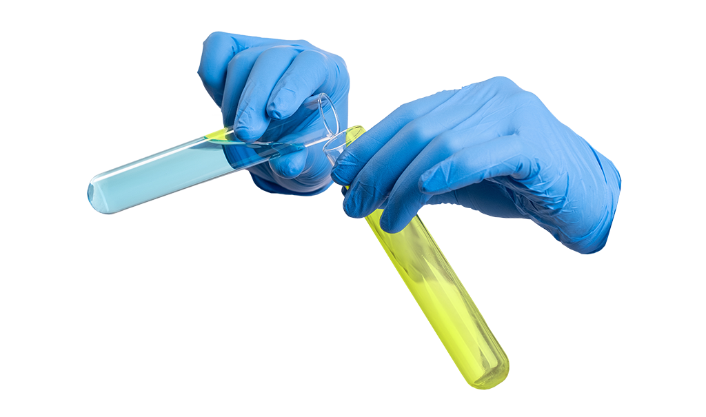 A pair of hands wearing blue latex gloves mixes two vials of blue and green liquid.