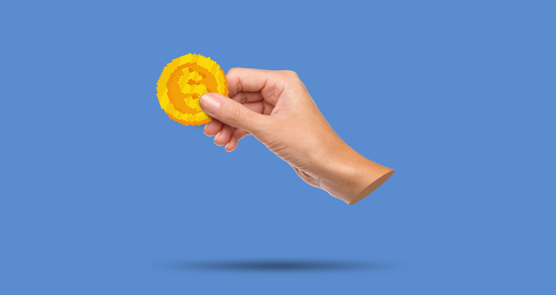 A hand holding a pixelated token in front of a blue backgorund.